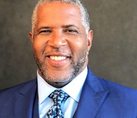 Robert F. Smith smiles while wearing a white shirt, patterned tie and blue suit and vest in front of a gray background